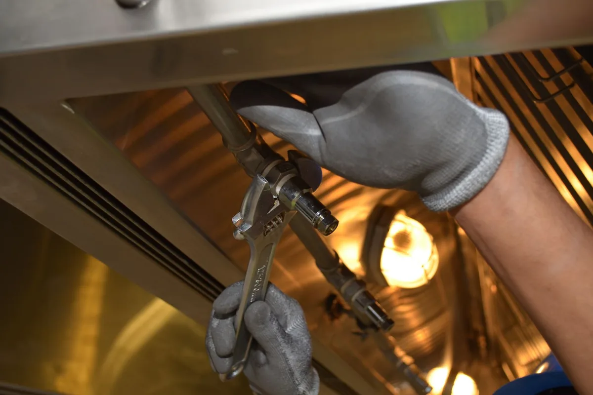 Plumber in work gloves using an adjustable wrench on a pipe fitting under a sink
